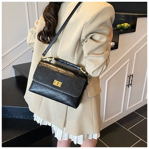 Detail of black quilted crossbody bag with gold twist lock on beige blazer outfit