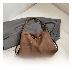 Détail d'un grand sac bandoulière en daim marron avec sangle en cuir sur un blazer gris