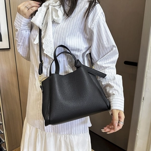 Sac à main noir en cuir grainé avec détails dorés porté par un mannequin en tenue