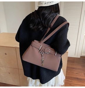 Detail of tan matte leather shoulder bag featuring decorative belt buckle and key charm