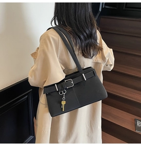 Detail of black matte underarm bag with silver buckle and gold key charm on beige trench coat