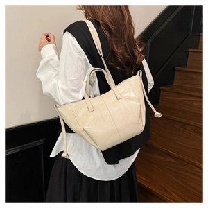 Detail of beige oil-wax leather tote bag showing glossy texture and drawstring side ties