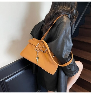 Detail of mustard yellow underarm bag with silver buckle and key charm on model