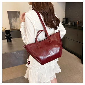 Detail view of large dark red tote bag in glossy PU leather shown on person's shoulder