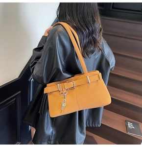 Detail of yellow shoulder bag with buckle straps and key charm on model in black leather jacket