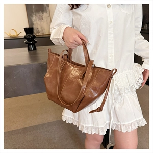Detail view of a brown glossy tote bag with adjustable side straps on a shoulder strap