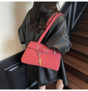 Close-up of coral pink shoulder bag featuring decorative buckle and metal key charm