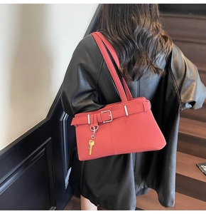 Detail view of red faux leather shoulder bag with buckle strap and gold key charm