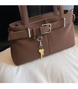 Detail view of dark brown leather tote bag with silver buckles and a gold key pendant