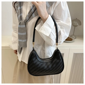 Detail of black woven crescent bag with gold hardware held by a model in casual wear