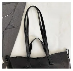 Close-up of black PU leather tote bag with dual handles on a white background