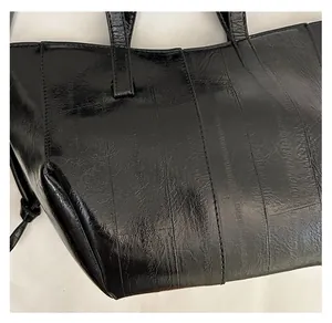 Detail of glossy black leather tote bag featuring vertical stitching and textured finish