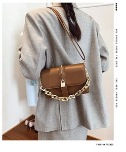 Detail of a brown leather crossbody bag with gold chain and buckle on a grey suit