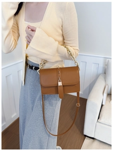Detail of caramel crossbody bag with gold chain strap and mini padlock on a model