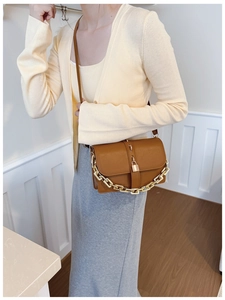 Detail of caramel brown crossbody bag with gold square lock and decorative metal chain