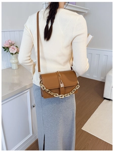Detail of a brown leather crossbody bag with a gold lock and a thick gold chain strap
