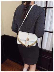 Close-up of white crossbody bag featuring a bold gold chain and elegant metal clasp