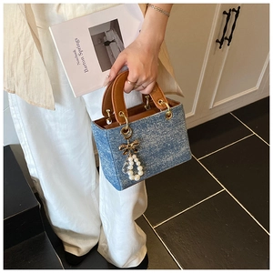 Detail of light blue denim handbag with brown leather handles and pearl bow charm