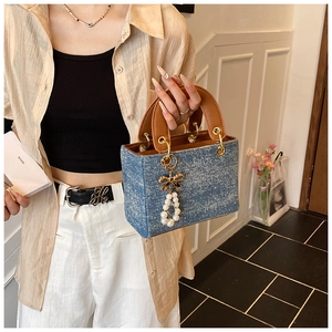 Blue denim crossbody bag featuring brown leather handles and pearl bow charm accessory