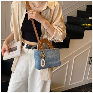 Detail of blue denim crossbody bag with pearl bow pendant and brown leather handle