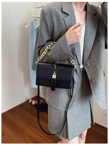 Detail of black leather handbag with a chunky gold chain strap and square metal lock
