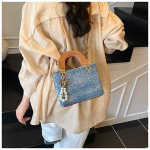 Blue denim crossbody bag with brown leather handles and a pearl bow charm detail