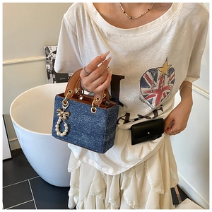 Close-up of blue denim mini bag with pearl bow charm and brown leather handle