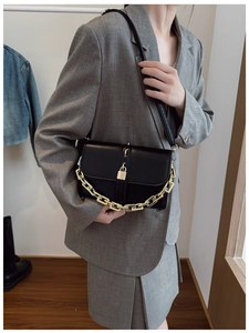 Detail of black crossbody bag featuring gold chain strap and lock on a grey suit