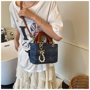 Detail of denim bag with tiny dots, brown leather handle and pearl bow charm