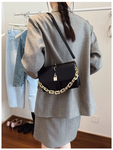 Detail of black leather flap bag with gold chain strap and square buckle on grey suit