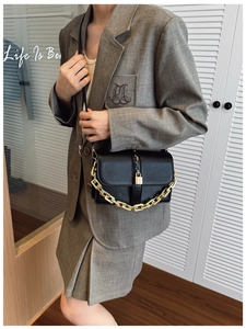 Detail of black leather shoulder bag with gold chain and metal buckle on model