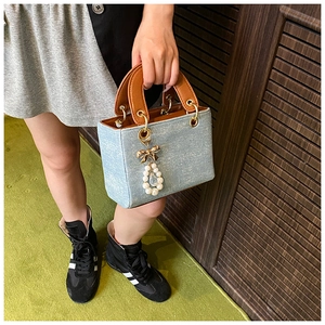 Detail of denim handbag with rhinestone finish, brown leather handle and gold bow charm