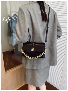 Detail of a black crossbody bag with chunky gold chain and metal lock on a model