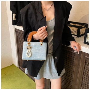 Detailed view of denim handbag with golden bow pendant and pearl teardrop charm