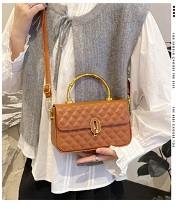 Detail of a brown quilted leather crossbody bag with bamboo handle and gold hardware