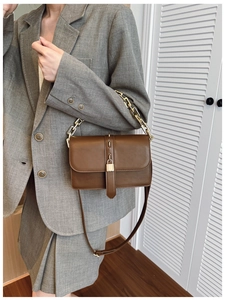 Close-up of brown leather crossbody bag with gold lock and chain strap on grey outfit