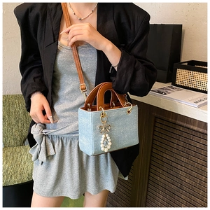 Detail of light blue denim mini bag with brown leather handles and pearl bow charm