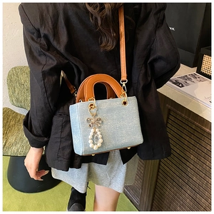 Detail of denim mini bag with caramel leather handle and pearl bow charm on model