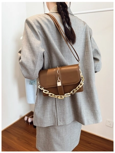 Brown leather crossbody bag with gold chain and lock detail on model in minimalist interior