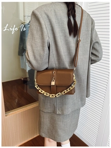 Close-up of brown leather crossbody bag with bold gold chain and buckle on suit