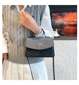 Close-up of black crossbody bag with V-quilted texture and elegant gold butterfly clasp