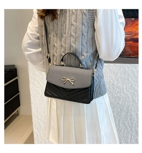 Detail of grey and black crossbody bag with gold bow clasp and V-quilted texture