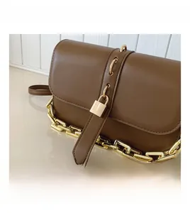 Detail of brown leather bag featuring golden chain strap and padlock hardware decoration