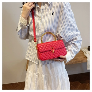 Detail of red quilted crossbody bag with a golden bamboo handle and metallic clasp closure