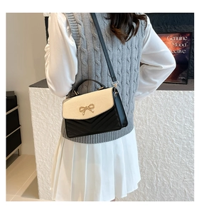Detail of minimalist small square bag with woven beige flap and gold bow clasp