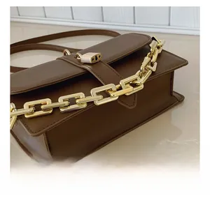 Detail of brown leather bag showing gold buckle and chunky metal chain strap close-up