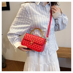 Detail of red quilted handbag with golden bamboo handle and rotating lock closure