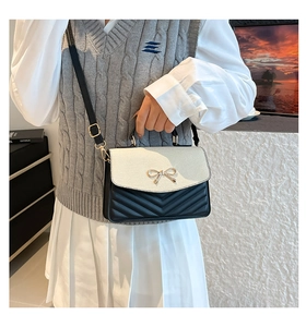 Détail du sac à main contrasté avec surpiqûres en V, nœud doré et rabat magnétique