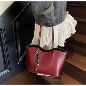 Detail of dark red faux leather tote bag featuring a woven rope charm and golden bell