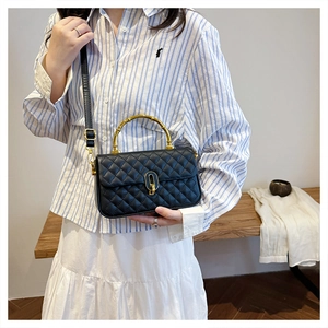 Detail of black quilted crossbody bag with golden bamboo handle and turn-lock closure